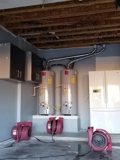 Two tank water heaters above a garage floor being dried by air movers