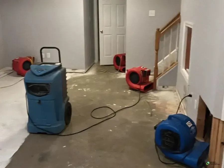 A dehumidifier and air movers drying a hallway next to a staircase